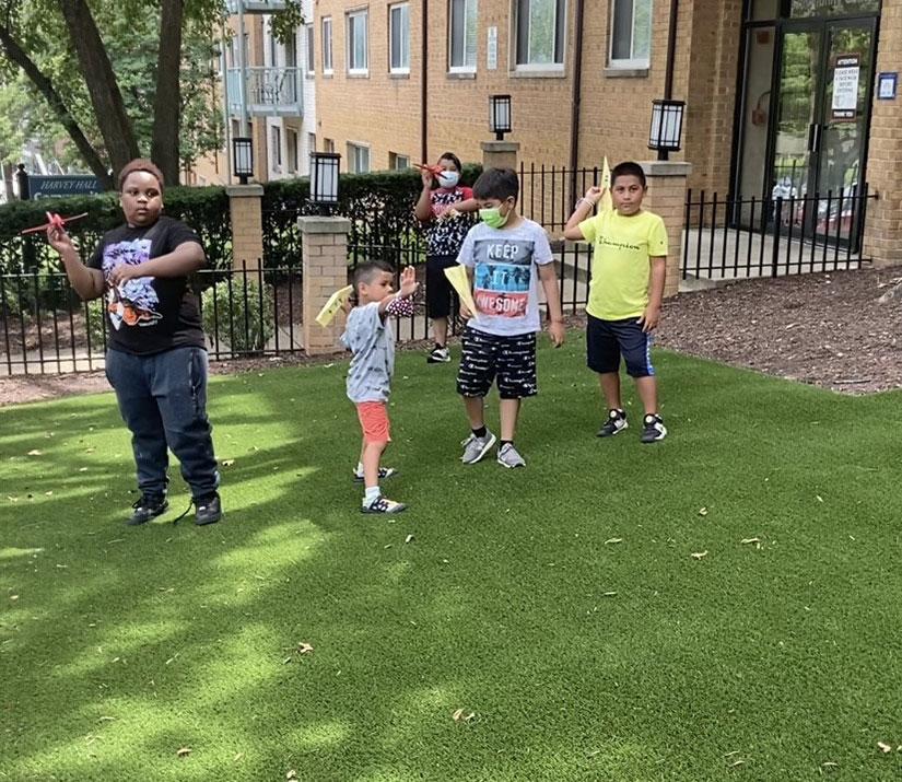 Multicultural elementary-aged kids testing homemade paper airplanes outside at summer youth program