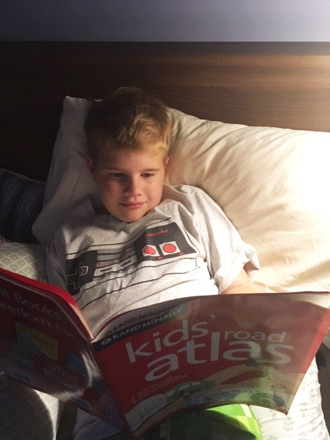 Young boy reading Rand McNally Kids’ Road Atlas in bed