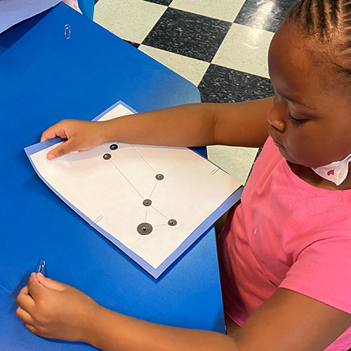 Young child making constellations in summer program