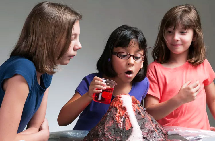 three girls looking at a homemade volcano with excitement