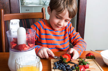 boy cutting fruit and there is a blender