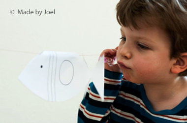 Boy blowing on a paper fish on a string.