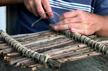 A child's hands building a stick raft.