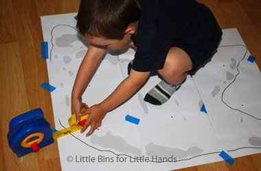 Child measuring out a dinosaur footprint on paper.