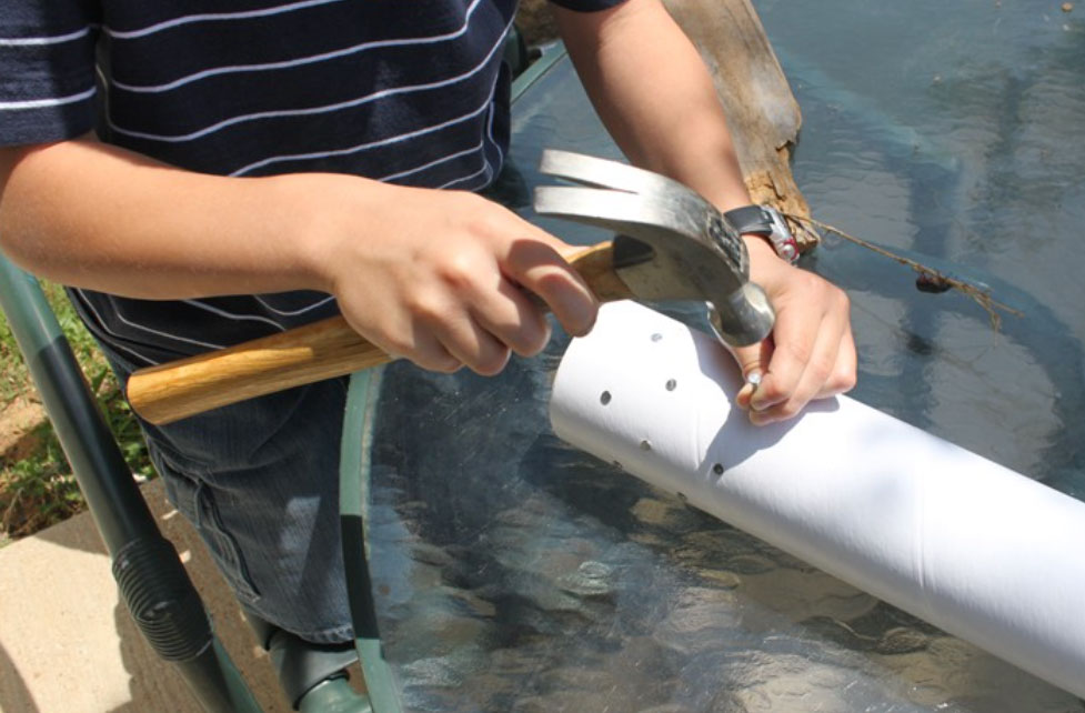 child hammering nails into a tube to make a rainstick