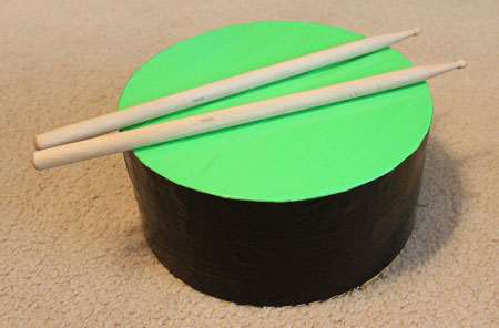 photo of a homemade black and green drum and two drumsticks