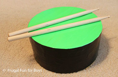 photo of a homemade black and green drum and two drumsticks