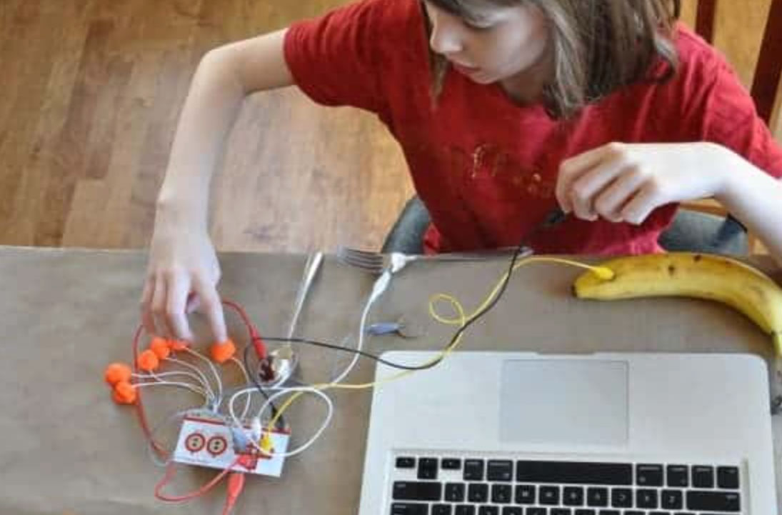 Young girl creating an invention from a banana, wires and a computer