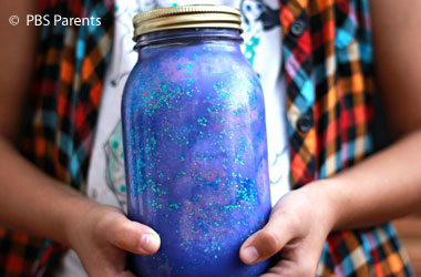 A child's hands holding a mason jar filed with swirled colors and glitter.