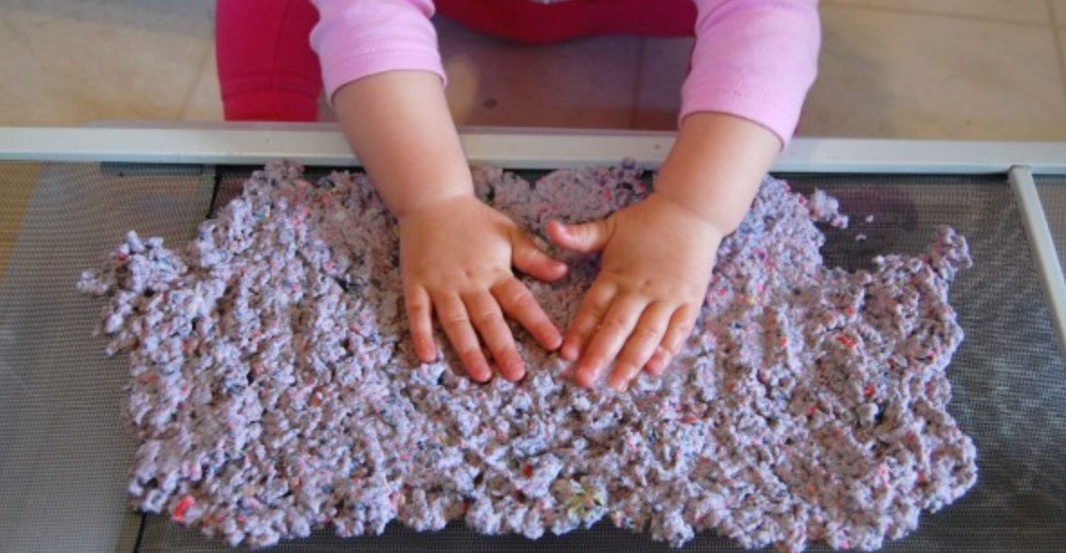 Young child patting slurry for homemade paper