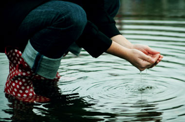 young child cupping water from a pond