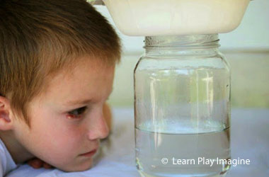 boy looking a a jar of water that has a bowl on top of it