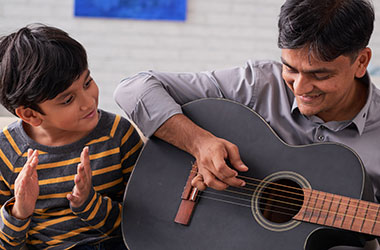 A man playing a guitar while a young boy claps along.