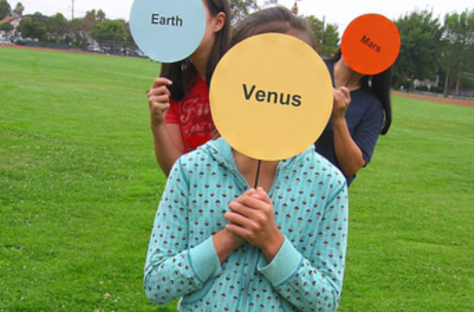 three children holding the names of planets in front of their faces