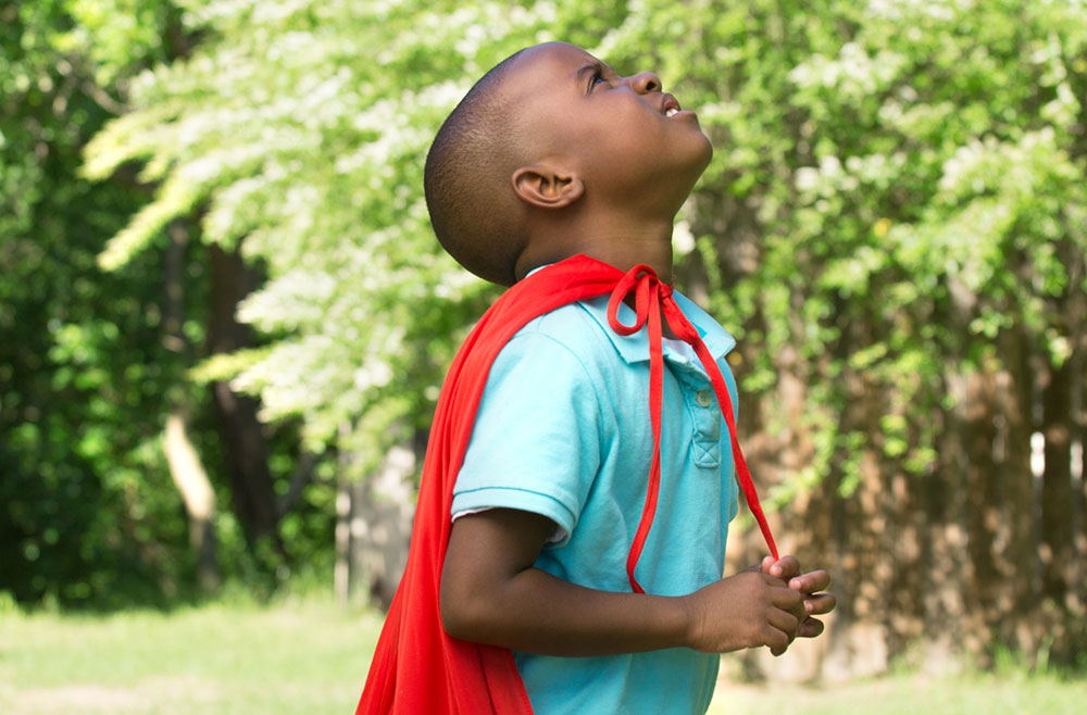 young child wearing a red superhero cape
