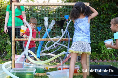 Kids attaching hoses and funnels to a chicken wire wall.