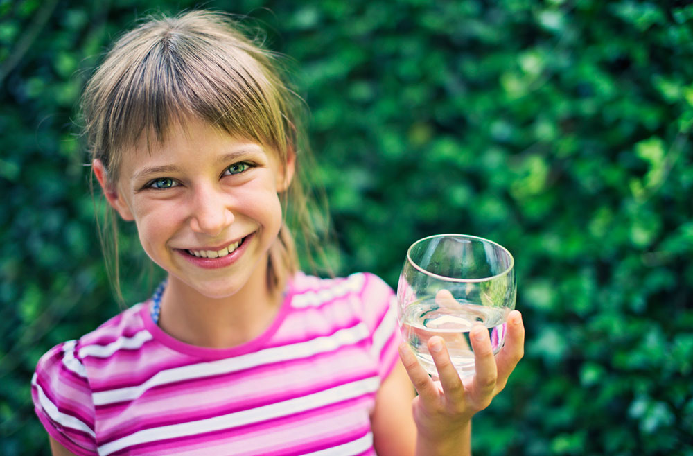 young girl in striped shirt holding a glass of water