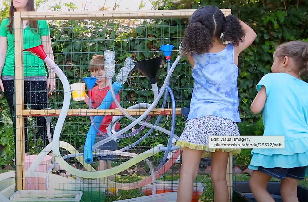 Kids attaching hoses and funnels to a chicken wire wall