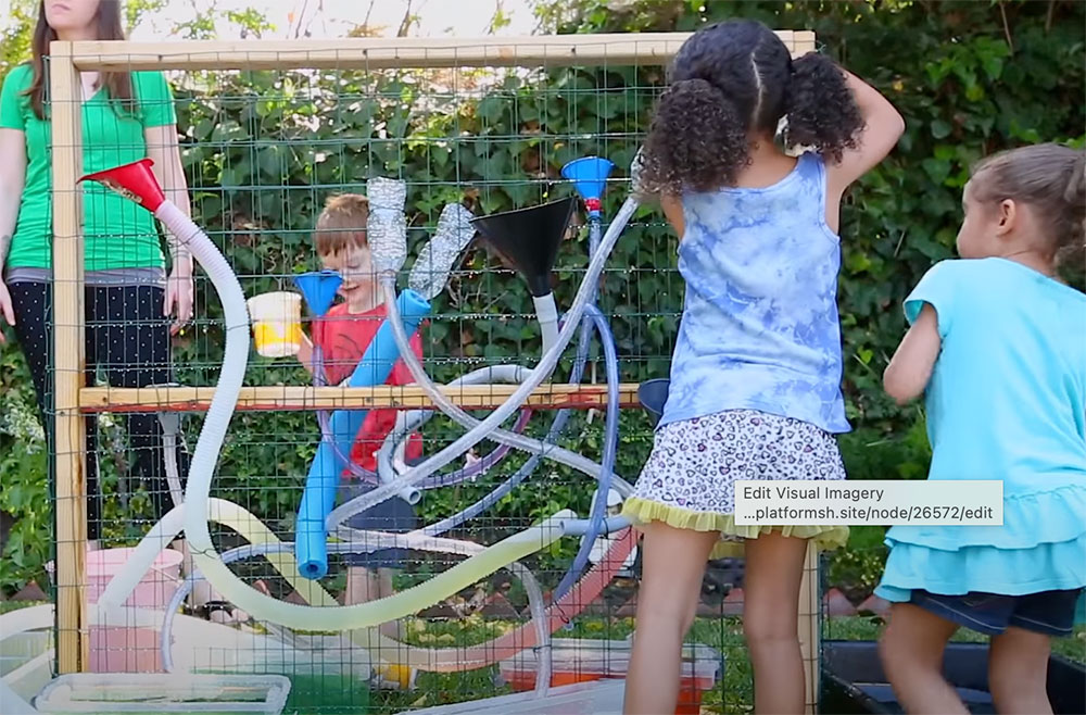 Kids attaching hoses and funnels to a chicken wire wall
