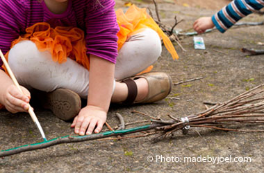 Child painting the handle of a bunch of sticks made to look like a broom.