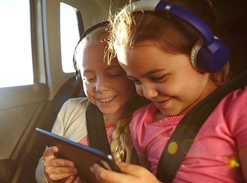two you girls wearing headphones and looking at a tablet device while in a car