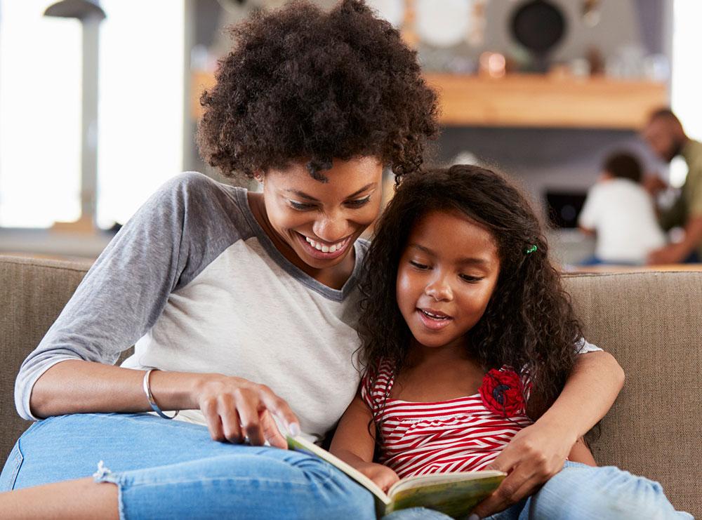 Mother reading a book to her elementary school-aged daughter at home