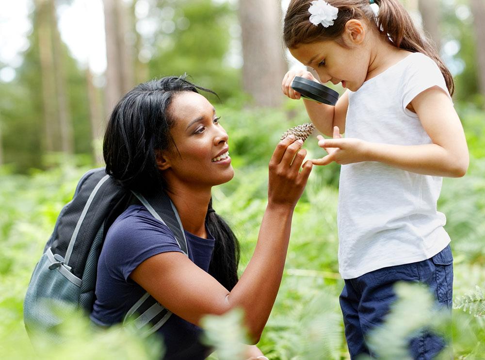 Mother and daughter examining a pine cone up close outside