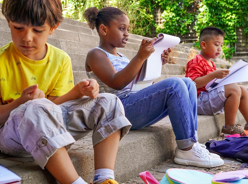 Diverse group of three elementary-aged kids writing outside