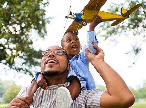 Young boy holding a toy airplane rides on his father's back