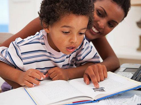 Woman pointing out illustrations in a book to a child.
