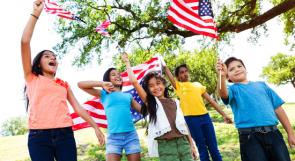 multicultural group of children outside waving U.S. flags