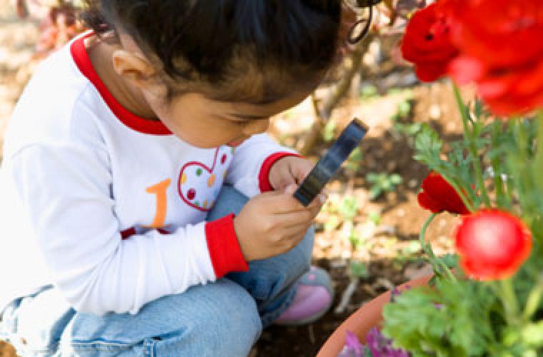 young child looking at a plant through a magnifying glass