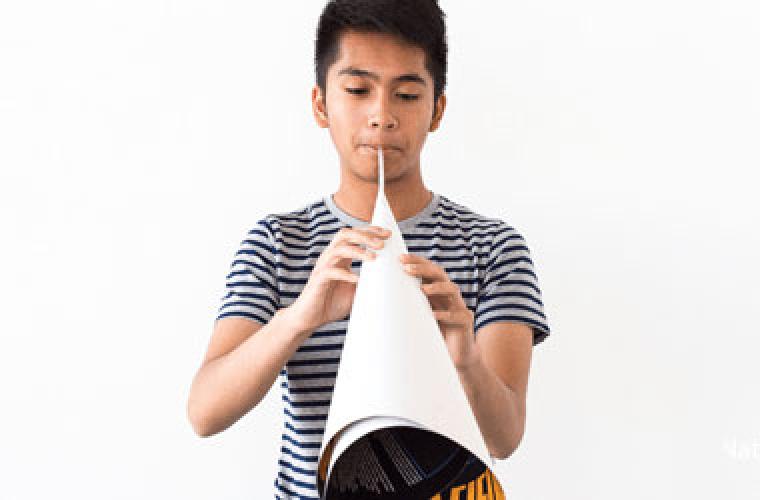 photo of boy blowing through the end of a paper cone