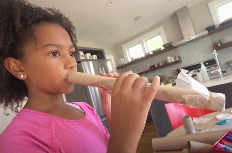 Young girl trying out a homemade kazoo made from a cardboard tube