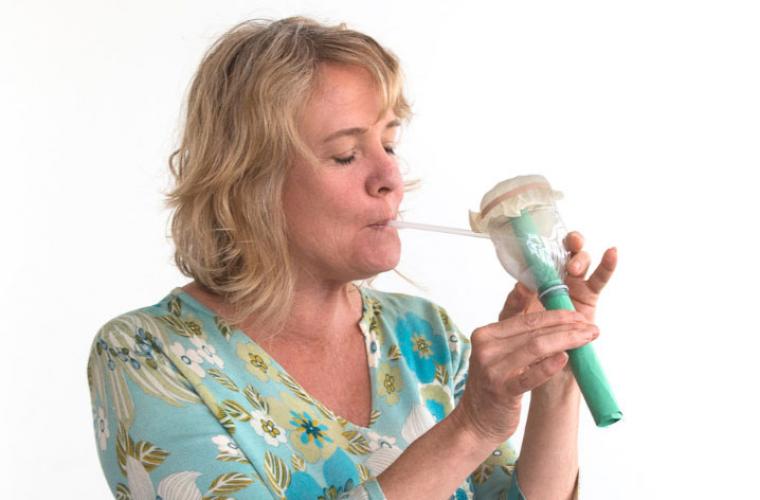 woman blowing on a DIY musical pipe made from a water bottle