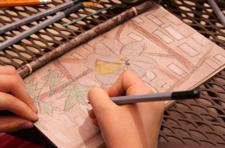 child drawing nature scene in homemade journal