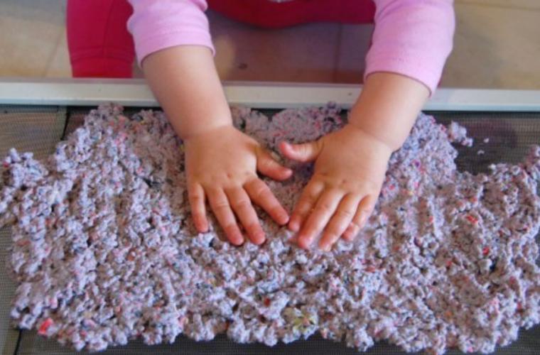 Young child patting slurry for homemade paper