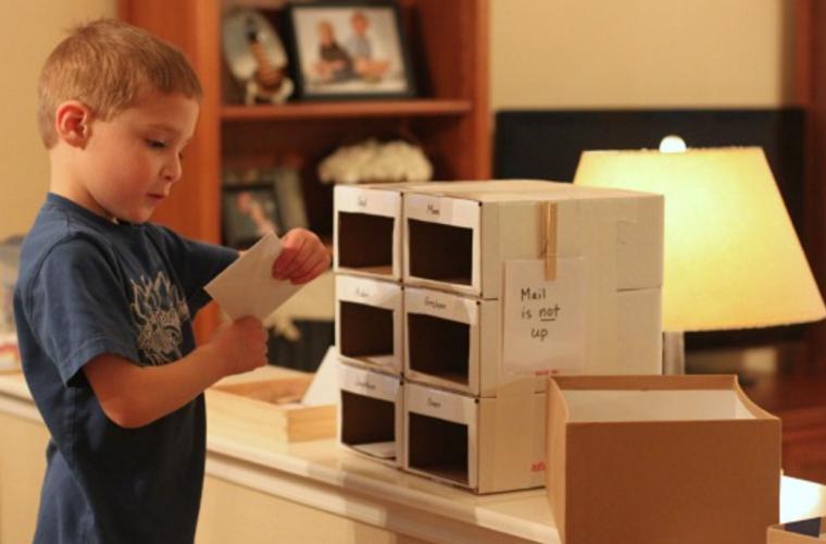 young boy sorting mail into cardboard mailbox slots