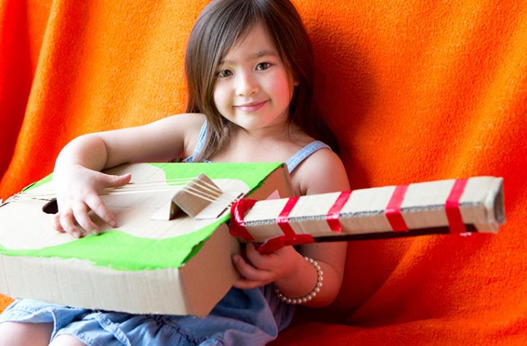 young girl holding homemade cardboard guitar