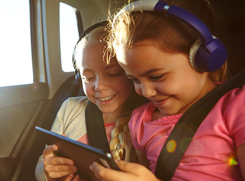 two girls wearing headphones and looking at a tablet two you girls wearing headphones and looking at a tablet device while in a car